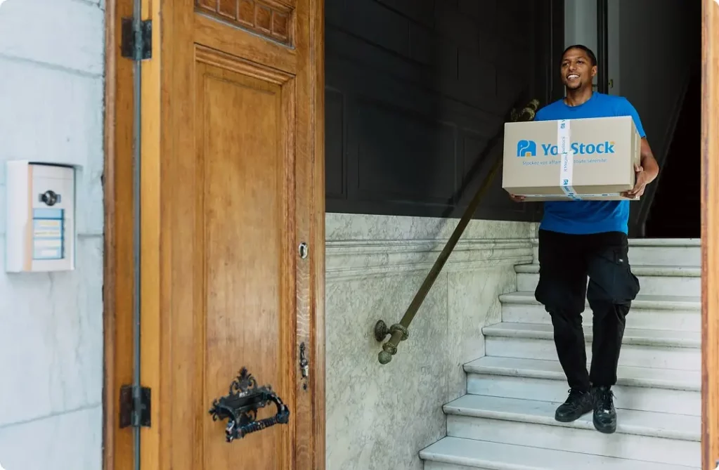 A YouStock mover descends the stairs with a moving box in his hands