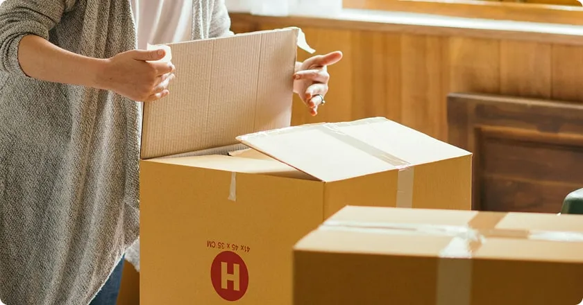 A young woman opens a moving box on a bed.