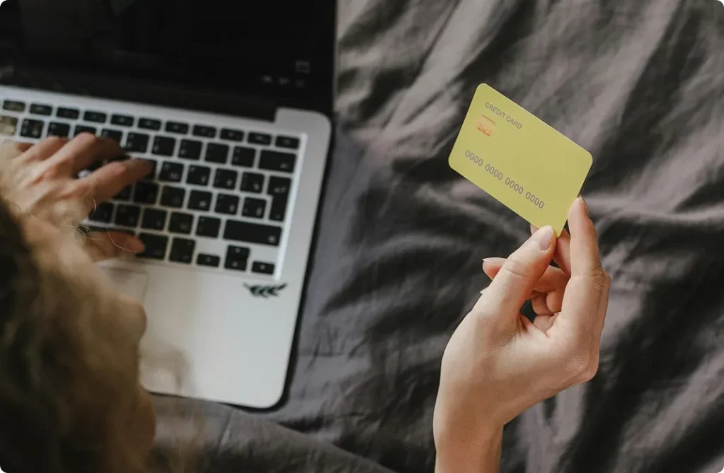 Jeune femme tenant une carte de crédit à côté d'un ordinateur portable
