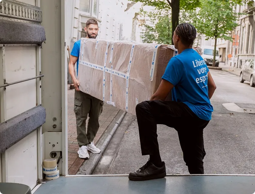 Deux professionnels YouStock portent un meuble emballé et protégé à l'arrière d'un camion de déménagement