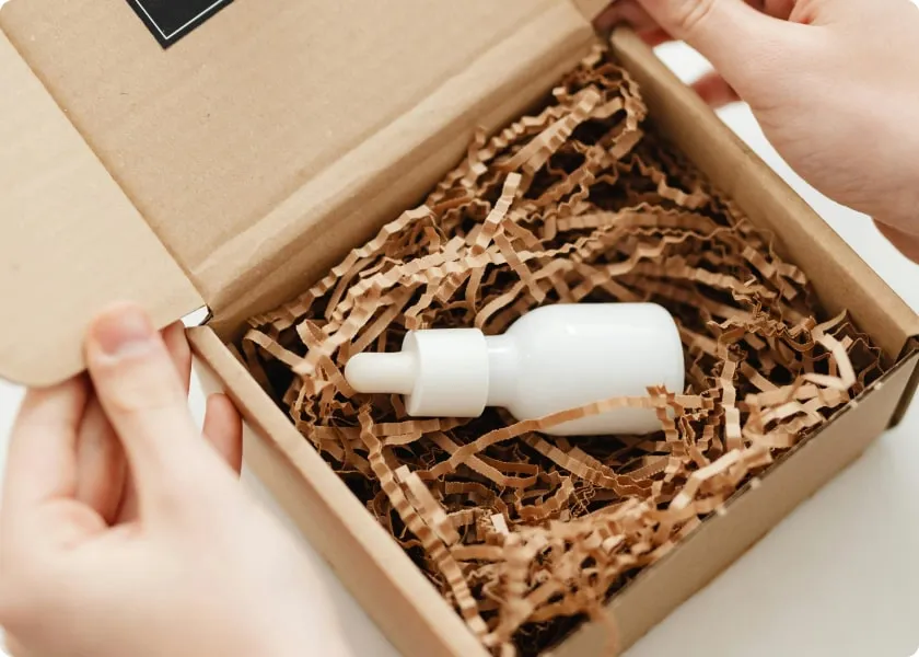 Small white bottle of serum in a cardboard box filled with crimped dunnage
