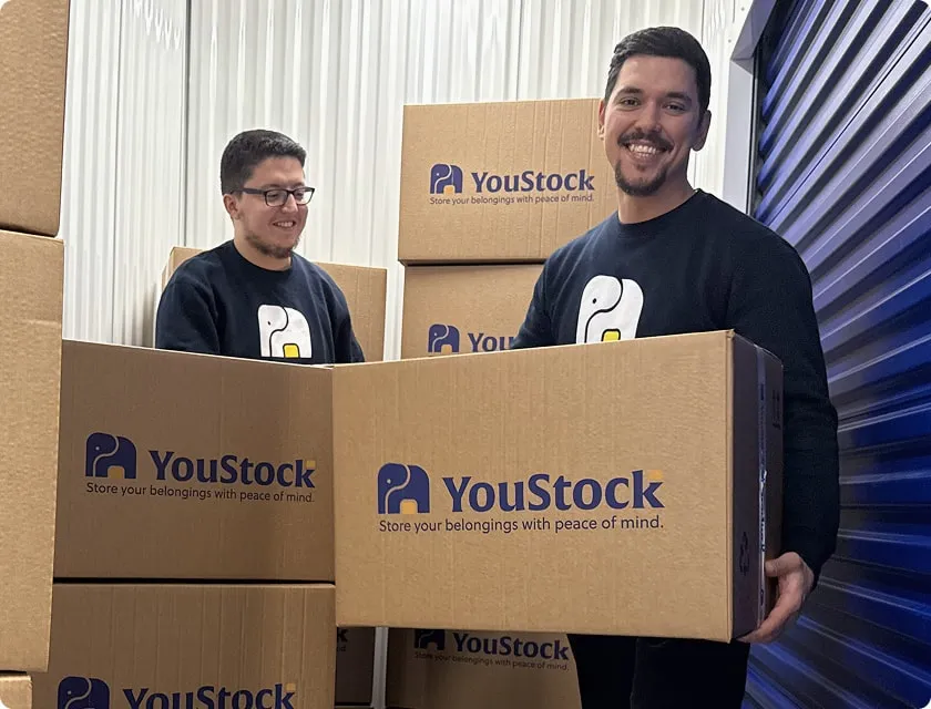 Two YouStock movers carrying a YouStock branded cardboard box - Store your belongings with peace of mind.