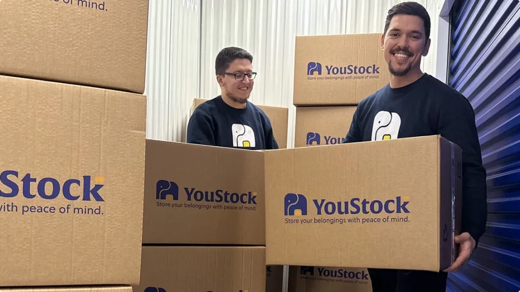 Two YouStock movers each carry a YouStock branded cardboard box - Store your belongings with peace of mind.