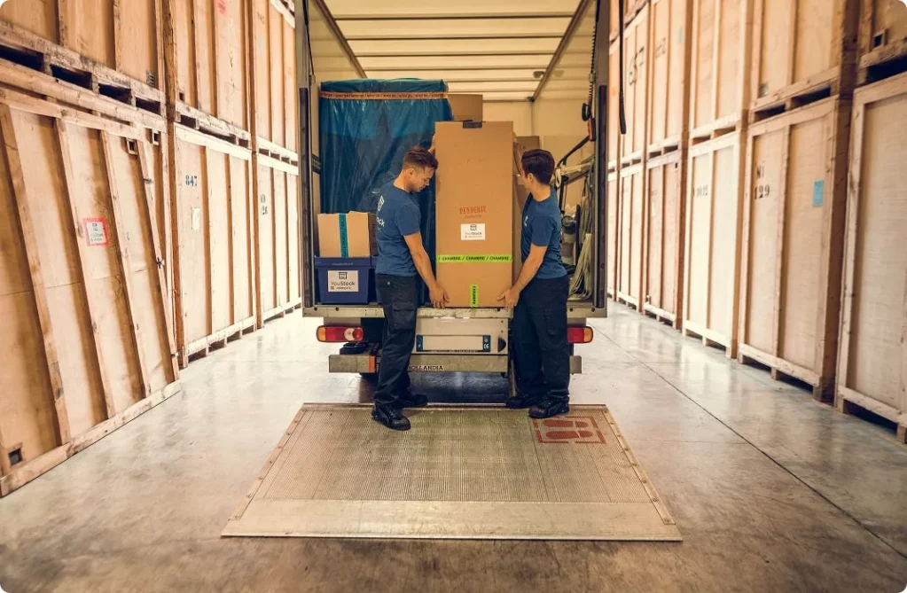 Two removal men unload a removal lorry in the middle of a storage warehouse