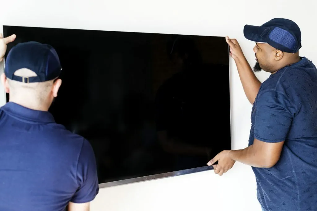 Deux déménageurs décrochent l'écran plat de télévision du mur