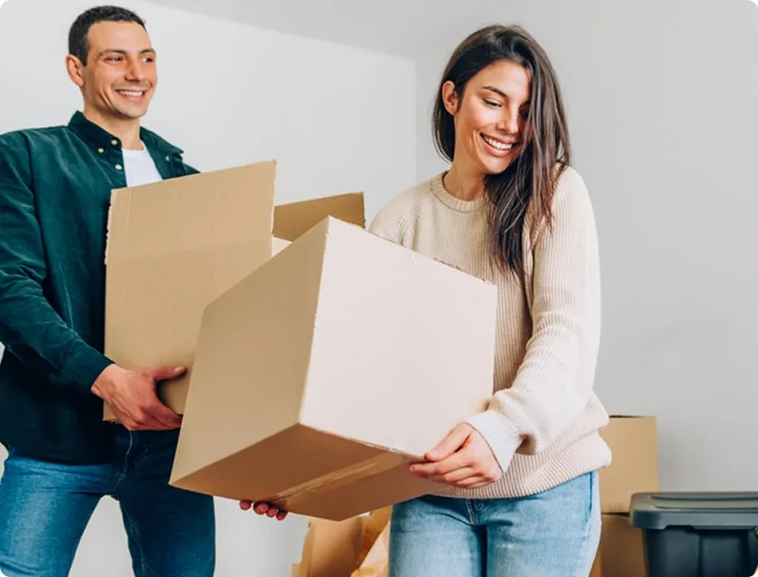 Un homme et une femme souriants portent chacun un carton de déménagement