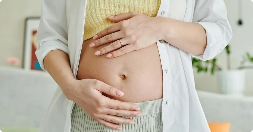 A pregnant woman with her hands resting on her exposed belly.