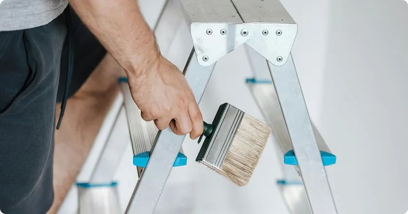 A man climbs a stepladder holding a paintbrush.