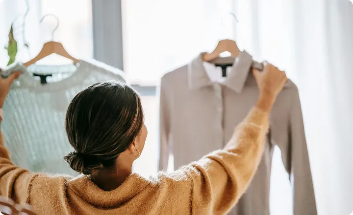 Une jeune femme compare 2 hauts sur cintres