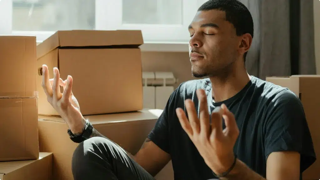 Jeune homme méditant assis au milieu de cartons