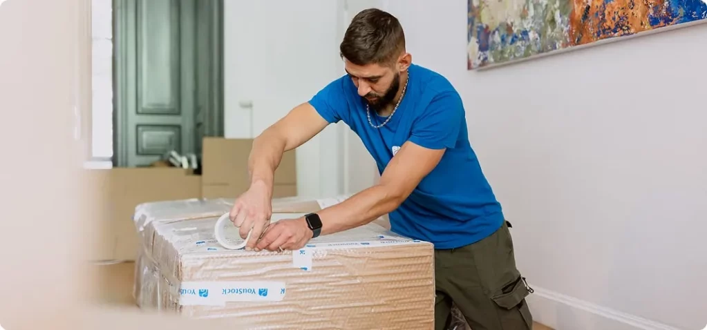 Un déménageur YouStock scotch un carton de déménagement après l'avoir emballé