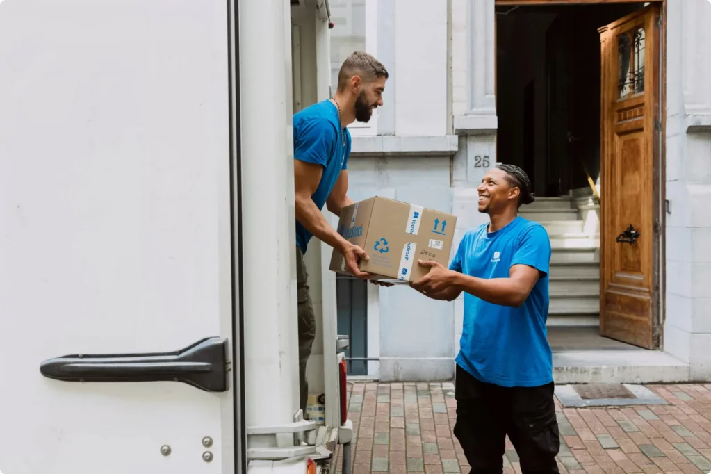 Two YouStock movers pass each other a storage box.