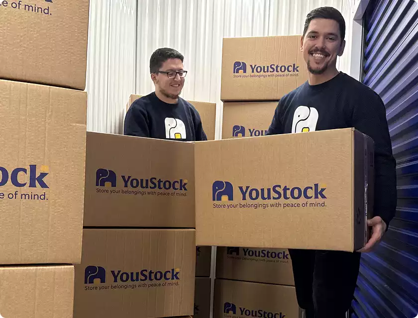 Two YouStock movers each carry a YouStock branded cardboard box - Store your belongings with peace of mind.