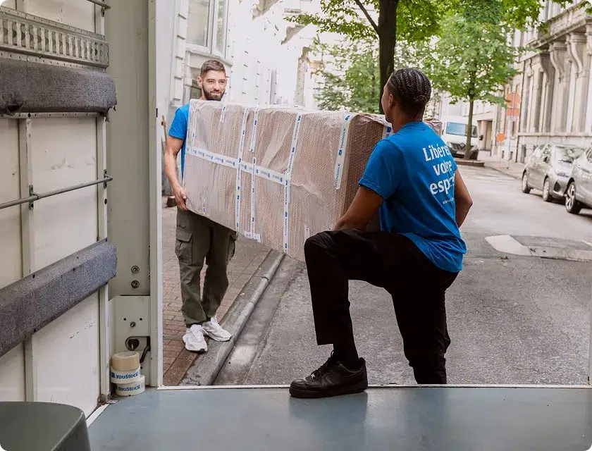 Two YouStock movers load a packed piece of furniture onto the back of a moving truck