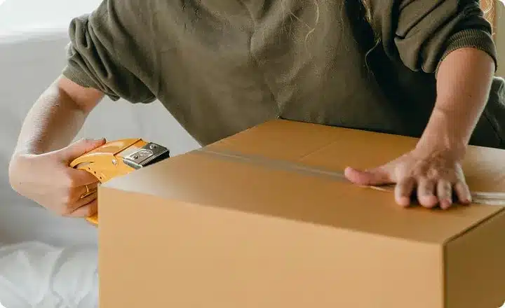 A woman seals a cardboard box with tape.