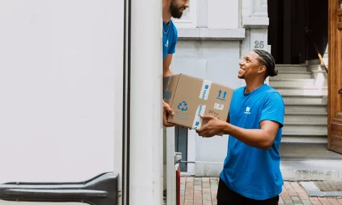 Two YouStock movers pass around a storage box in the back of a moving truck.