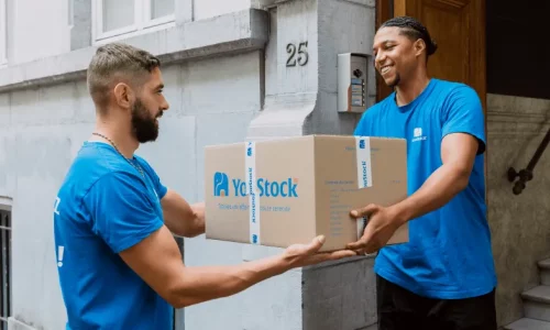 Two YouStock removal men pass a moving box between them.