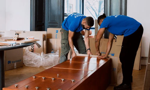 long-term-storage-removal-travelling Two removal men carefully pack and protect a large piece of wooden furniture for storage.