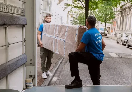 Two YouStock professionals carry a wrapped and protected piece of furniture to put it in a truck through the streets of Paris