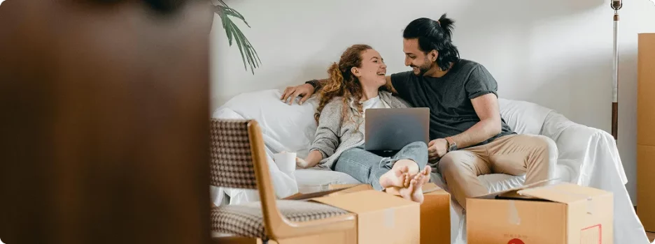 A young couple is sitting on a sofa protected by moving boxes.
