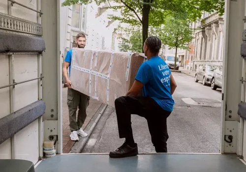 Deux déménageurs YouStock portent un meuble emballé et protégé à l'arrière d'un carton de déménagement